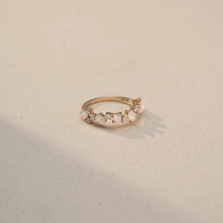 Side view of a Multi-Shape Diamond Eternity Band in 14KT Yellow Gold, featuring mixed oval, princess, and round lab-grown diamonds in a scattered cluster design. Captured against a beige backdrop with soft shadow.