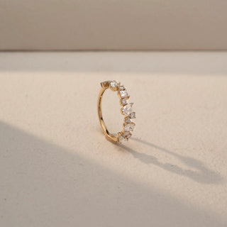 Angled view of a Multi-Shape Diamond Eternity Band in 14KT Yellow Gold, featuring mixed oval, princess, and round lab-grown diamonds in a scattered cluster design. Captured against a beige backdrop.
