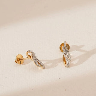 Angled view of triple wave diamond earrings featuring intertwined yellow gold curves with pavé-set round lab-grown diamonds and screw-back posts, displayed on a soft neutral background.