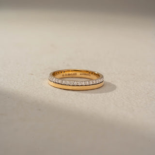 Front view of a diamond wedding band in 14 KT Yellow Gold, featuring a row of round lab-grown diamonds set within a sleek channel-style design, displayed against a beige backdrop.