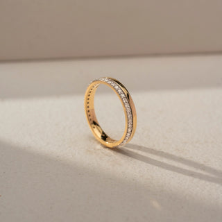 Angled view of a diamond wedding band in 14 KT Yellow Gold, featuring a row of round lab-grown diamonds set within a sleek channel-style design, displayed against a beige backdrop.
