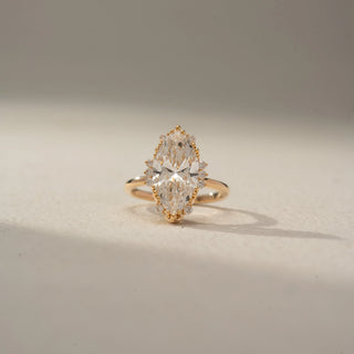 Front view of a marquise halo engagement ring in 14 KT Yellow Gold, featuring a marquise-cut lab-grown diamond surrounded by a delicate halo of round diamonds, displayed against a beige backdrop.