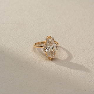 Side view of a marquise halo engagement ring in 14 KT Yellow Gold, featuring a marquise-cut lab-grown diamond surrounded by a delicate halo of round diamonds, displayed against a beige backdrop.