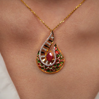 Closeup view of an exquisite female pendant, modelled on a neckline, features a captivating teardrop design, showcasing a vibrant ruby encircled by a delicate halo of Lab-Grown diamonds. The intricate goldwork is adorned with emerald enamel accents, adding a touch of elegance. This stunning statement piece is crafted in 14 KT yellow gold and boasts a total diamond weight of 0.47 carats and the total weight of the pendant is 5.12 grams