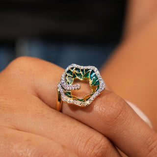 A close-up top view of an abstract diamond 14 KT female ring of size 12 modelled on a hand. The ring features a vibrant coral-inspired motif adorned with multi-coloured enamel and set with 0.35 carats of sparkling lab-grown diamonds. The 14KT yellow gold band complements the ring's playful and colourful design.