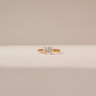 Front view of Oval Diamond Solitaire Ring in 14KT Yellow Gold, featuring an oval-shaped diamond. Captured against a beige backdrop.
