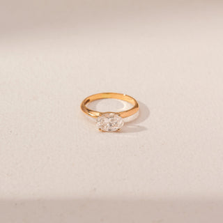 Top view of Oval Diamond Solitaire Ring in 14KT Yellow Gold, featuring an oval-shaped diamond. Captured against a beige backdrop.