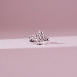 Front angle view of a 14KT white gold double floral cluster diamond ring with two pear-shaped diamond blossoms and a curved pavé diamond band, set against a soft pink background.