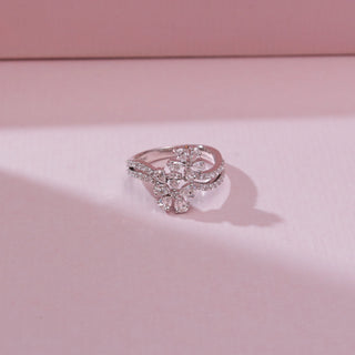 Angled top view of a 14KT white gold double floral cluster diamond ring with pear-shaped diamond petals and a split pavé diamond band, displayed on a soft pink background.