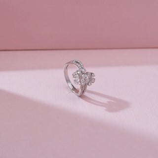 Side angle view of a 14KT white gold double floral cluster diamond ring with pear-shaped diamond petals and a curved pavé diamond band, set on a soft pink background.