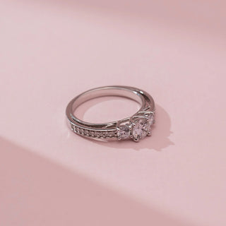 Top view of Reia’s 14 KT White Gold Threefold Promise Solitaire Diamond Ring, showing three round diamonds on a pavé band. Set against pink, it highlights high-shine, symmetrical elegance.