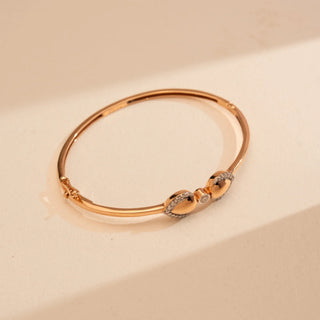 Top view of Reia’s 14 KT Rose Gold Radiant Heart Diamond Bangle. Captured on a cream backdrop, it highlights the sleek 14 KT rose gold foundation and contemporary silhouette.