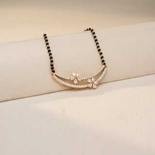 Angled view of a floral diamond mangalsutra necklace in 14 KT Dual Gold, featuring curved pavé-set diamond arcs accented with marquise-shaped floral motifs and black bead chains, displayed on a beige backdrop