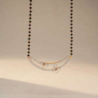 Front view of a floral diamond mangalsutra necklace in 14 KT Dual Gold, featuring curved pavé-set diamond arcs accented with marquise-shaped floral motifs and black bead chains, displayed on a beige backdrop