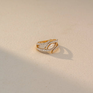 Side view of a marquise diamond wrap ring in 14 KT Yellow Gold, featuring a marquise-cut lab-grown diamond framed by intertwined pavé-set diamond bands in a layered open design, displayed against a beige backdrop.