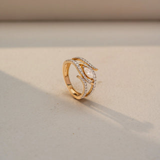 Angled view of a marquise diamond wrap ring in 14 KT Yellow Gold, featuring a marquise-cut lab-grown diamond framed by intertwined pavé-set diamond bands in a layered open design, displayed against a beige backdrop.