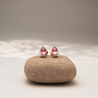 Front view of pear-shaped pink gemstone stud earrings in 14 KT Yellow Gold, featuring soft pink center stones framed with pavé diamond accents, displayed on a textured stone surface.
