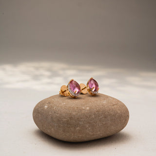 Side view of pear-shaped pink gemstone stud earrings in 14 KT Yellow Gold, featuring soft pink center stones framed with pavé diamond accents, displayed on a textured stone surface.