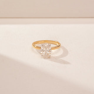 Close up view of a 14KT Yellow Gold diamond ring, featuring an oval-cut centre diamond and a plain gold band.