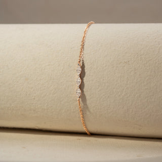 Close Up view of a diamond bracelet in 14 KT Rose Gold, featuring three marquise-shaped diamonds set along a delicate chain, displayed against a soft beige backdrop.