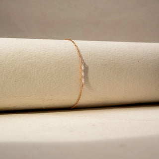 Side Up view of a diamond bracelet in 14 KT Rose Gold, featuring three marquise-shaped diamonds set along a delicate chain, displayed against a soft beige backdrop.