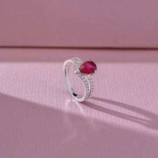 Side angled view of red diamond ring in white gold, featuring a pear-shaped vibrant red centre stone with a split diamond-studded band of round lab-grown diamonds. Set on a soft pink backdrop, it highlights bold sparkle.