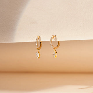 Side view of marquise lab-grown diamond hoop earrings in 14KT Yellow Gold, featuring diamond-studded hoops with suspended marquise-cut diamond drops. Captured against a beige backdrop, the elegant design radiates timeless sparkle.