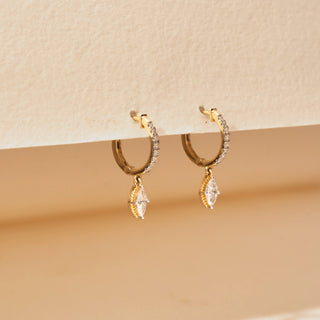Angled view of marquise lab-grown diamond hoop earrings in 14KT rose Gold, featuring diamond-studded hoops with suspended marquise-cut diamond drops. Captured against a beige backdrop, the elegant design radiates timeless sparkle.