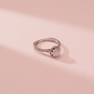 Top-down view of Reia’s 14 KT White Gold Classic Halo Solitaire Diamond Ring. It showcases the brilliant round center diamond, sparkling halo, and diamond-set band against a soft pink backdrop.