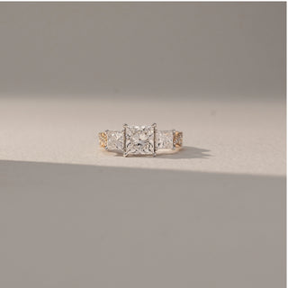 Front view of Princess Three Stone Diamond Ring in 14KT Yellow Gold, featuring a centred princess-cut lab grown diamond with square side stones. Set on a beige backdrop, the design highlights symmetry and brilliance.
