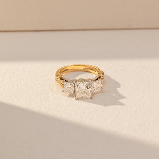 Top view of Princess Three Stone Diamond Ring in 14KT Yellow Gold, featuring a centred princess-cut lab grown diamond with square side stones. Set on a beige backdrop, the design highlights symmetry and refined brilliance.
