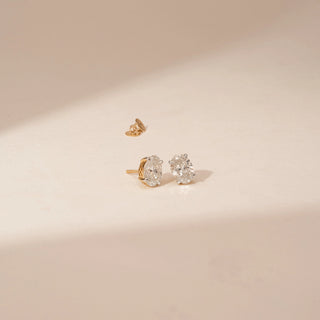 Angled view of 14KT Yellow Gold diamond earrings featuring oval centre diamonds with surrounding diamond accents in stud settings.