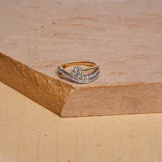 Set against a textured stone surface, this Réia ring showcases a layered gold band adorned with clusters of round lab grown diamonds, blending sparkle with a sculpted crossover design.