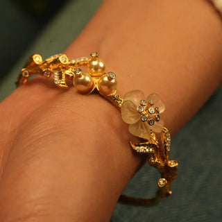 Floral motif bracelet featuring carved flower details, pearl accents, and small diamonds set along sculpted gold leaves in an ornate and elegant design.