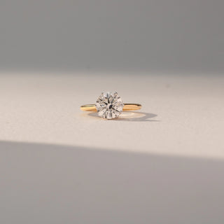 Front view of Round Solitaire Diamond Ring in 14KT Yellow Gold, featuring a centred round lab grown diamond in prong setting. Set on a beige backdrop, the design highlights classic brilliance and elegance.
