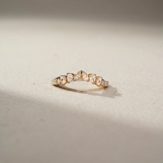 Front view of a curved diamond wedding band in 14 KT Yellow Gold, featuring alternating pear-shaped and round lab-grown diamonds in a graceful crown-inspired design, displayed against a beige backdrop.