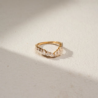 Side view of a curved diamond wedding band in 14 KT Yellow Gold, featuring alternating pear-shaped and round lab-grown diamonds in a graceful crown-inspired design, displayed against a beige backdrop.