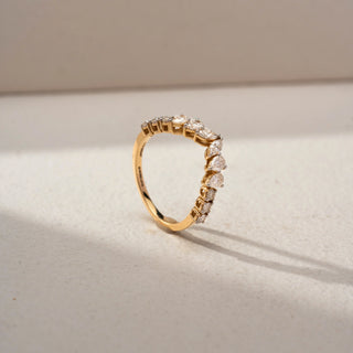 Angled view of a curved diamond wedding band in 14 KT Yellow Gold, featuring alternating pear-shaped and round lab-grown diamonds in a graceful crown-inspired design, displayed against a beige backdrop.