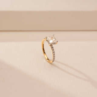 Angled view of a 14KT Yellow Gold diamond ring with a rectangular centre diamond in a four-prong setting and diamond-set shoulders.
