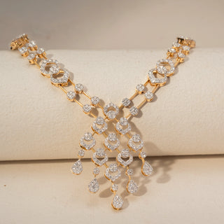 Side view of a diamond necklace in 14 KT Yellow Gold, featuring interlinked pavé-set oval motifs and a cascading diamond cluster centerpiece with pear-shaped drops against a soft beige backdrop.
