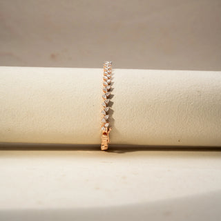 Front view of a diamond tennis bracelet in 14 KT Rose Gold, featuring a continuous row of heart-shaped diamonds in a sleek linear setting, displayed against a soft beige backdrop.
