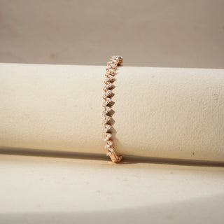 Close Up view of a diamond tennis bracelet in 14 KT Rose Gold, featuring a continuous row of heart-shaped diamonds in a sleek linear setting, displayed against a soft beige backdrop.