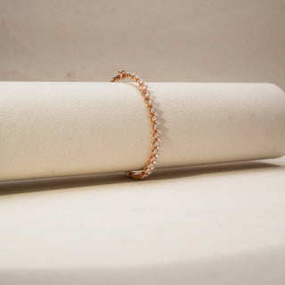 Side  view of a diamond tennis bracelet in 14 KT Rose Gold, featuring a continuous row of heart-shaped diamonds in a sleek linear setting, displayed against a soft beige backdrop.
