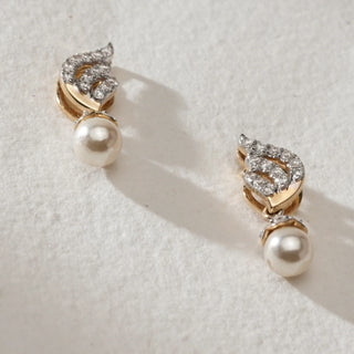 Close-up of Pearl Drop Spiral Diamond Earrings in 14KT Yellow Gold, featuring curved diamond-studded spiral tops with round pearl drops, displayed flat on a light textured surface.