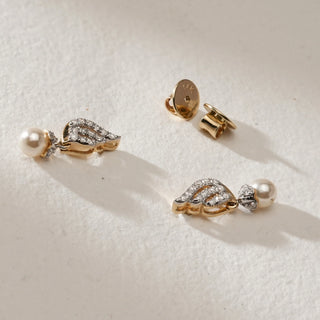 Pearl Drop Spiral Diamond Earrings in 14KT Yellow Gold, featuring a spiral diamond-studded design with luminous pearl drops, displayed flat on a beige textured surface alongside Bombay screw backs.