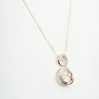 A side view of a female 14 KT female rose gold necklace of size 16  on a white background, featuring two interlocking circular pendants, the larger open circle and the smaller solid circle encrusted with round brilliant lab-grown diamonds totalling 0.638 carats set in a pavé style and total weight is 7.4 grams. The interconnected circles create an elegant yet modern infinity-inspired motif suspended from a rose gold cable chain necklace 