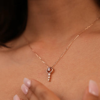 A view of a female necklace of size 16 secured through a spring lock gently modelled on a neckline, featuring a delicate 14 KT rose gold chain with a dangling pendant design. The necklace consists of a round brilliant-cut lab-grown diamond stud, suspending additional smaller round brilliant diamonds below, totalling 0.29 carats. The necklace showcases an elegant and minimalist style with a total weight being 2.63 grams