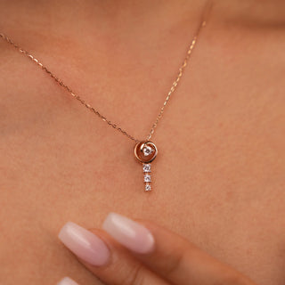 A view of a female necklace of size 16 secured through a spring lock gently modelled on a neckline, featuring a delicate 14 KT rose gold chain with a dangling pendant design. The pendant consists of a round brilliant-cut lab-grown diamond stud, suspending additional smaller round brilliant diamonds below, totalling 0.29 carats. The necklace showcases an elegant and minimalist style with a total weight being 2.63 grams.