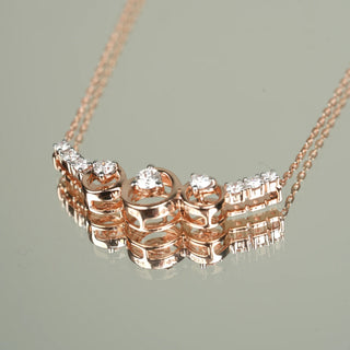 A view of an elegant 14 KT female rose gold necklace of size 16.8 secured through a spring lock laying on a mirror, featuring a curved bar pendant design adorned with round brilliant-cut lab-grown diamonds totalling 0.42 carats and the total weight being 3.76 grams. The diamonds are bezel-set in rose gold frames that alternate with polished rose gold circular links along the curved bar motif. The necklace has a delicate rose gold cable chain creating a graceful look.