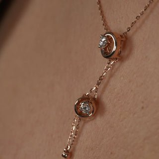 A close-up photo of a woman's neck wearing a delicate rose gold necklace showcasing the product adorned with two interconnected circles, each featuring a sparkling diamond in the centre. The image features the close-up front view of a swirling 14 KT Diamond Necklace, adorned with 0.21 carats of lab-grown diamonds, elegantly worn on the neck of the model of size 16 secured through a spring lock weighing a total of 3.28 grams